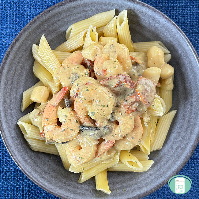 bowl of penne pasta topped with shrimp and scallops in a creamy yellow sauce