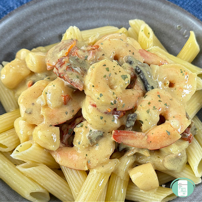 bowl of penne pasta topped with shrimp and scallops in a creamy yellow sauce