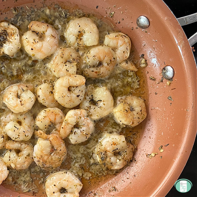shrimp cooking in butter with seasonings in a skillet