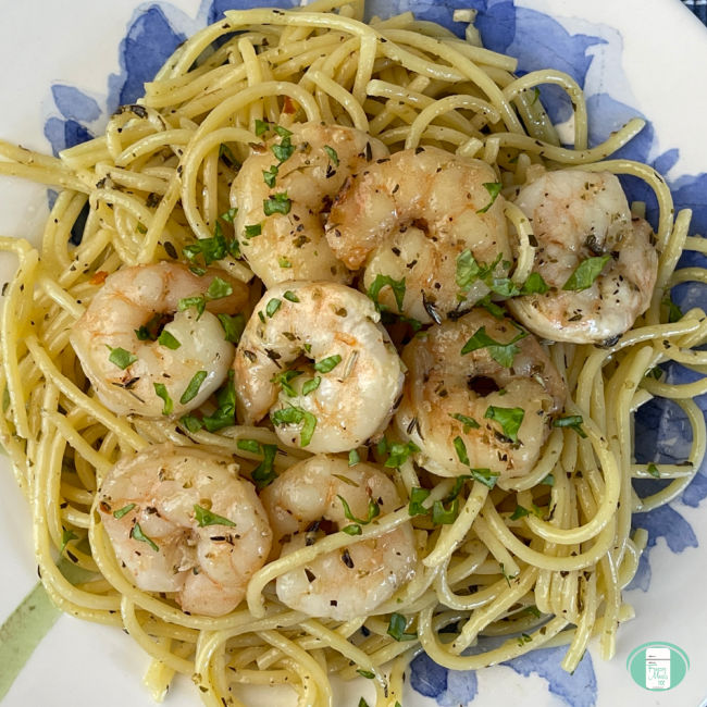 bed of spaghetti noodles on a plate topped with cooked shrimp sprinkled with parsley