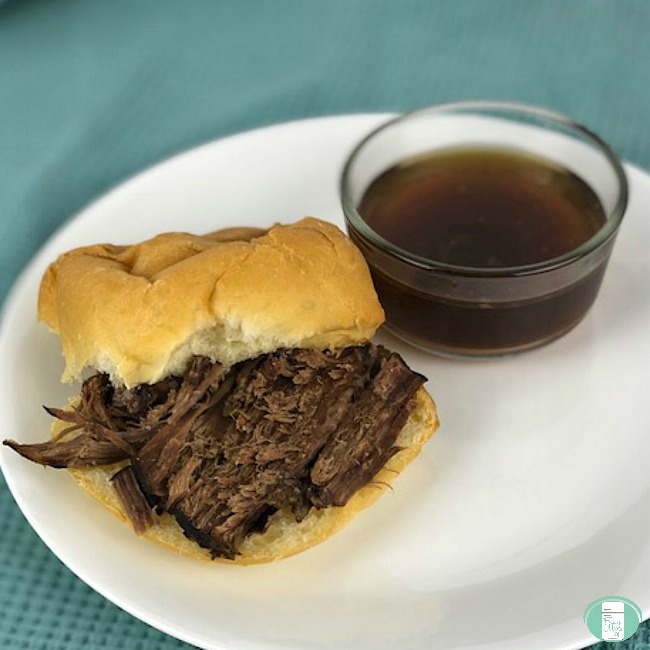 close up of beef on a bun with beef dip on the side