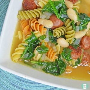 Broth soup with curly coloured pasta, white kidney beans, chopped tomatoes and spinach.