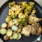 dark grey plate with halved baby potatoes, broccoli, cauliflower, and seasoned chicken