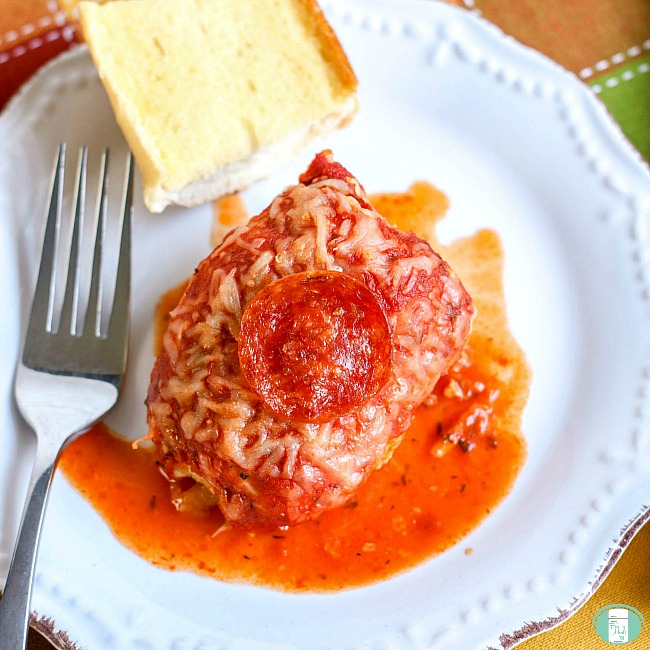 close up of a plate with pizza stuffed chicken, a fork and garlic bread