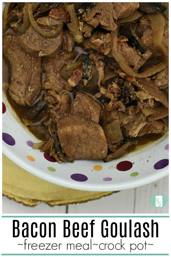 chunks of beef, bacon, mushrooms, and thin slices of onion in a brown sauce are in a white bowl with multi-colored polka dots. The text read "Bacon Beef Goulash freezer meal crock pot" #freezermeals101 #beefgoulash #crockpotmeal