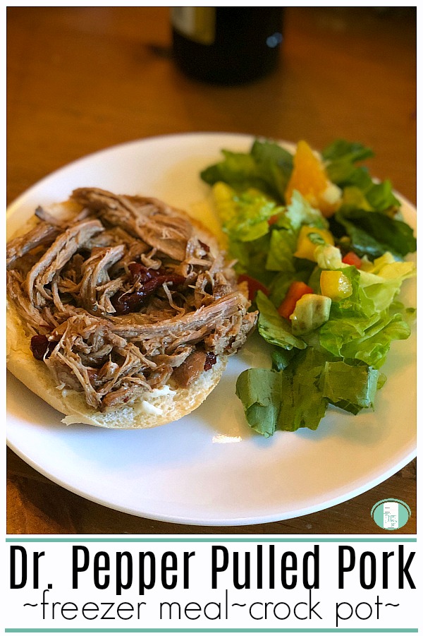 a bun sits on a white plate with shredded meat on top of it and a green salad beside it with a few tomato pieces. The text reads "Dr. Pepper Pulled Pork - freezer meal - crock pot" #freezermeals101 #pulledpork #crockpotfreezermeal