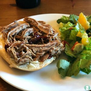 Pulled pork on an open-faced bun plated with a sie salad.