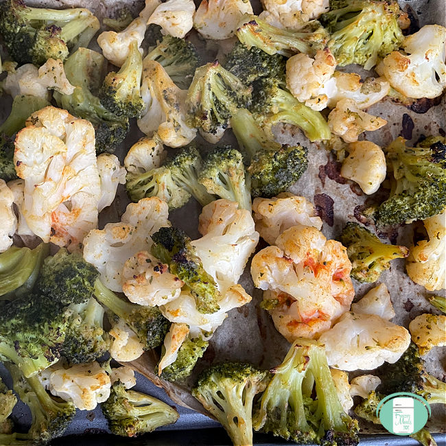 cooked cauliflower and broccoli on a parchment paper lined baking sheet