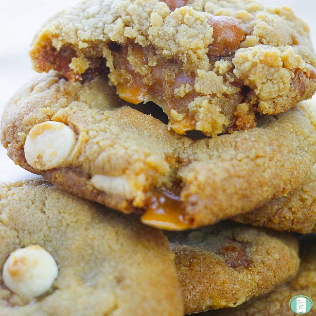 close up of caramel stuffed white chocolate chip cookies with the one on top broken in half and oozing with caramel
