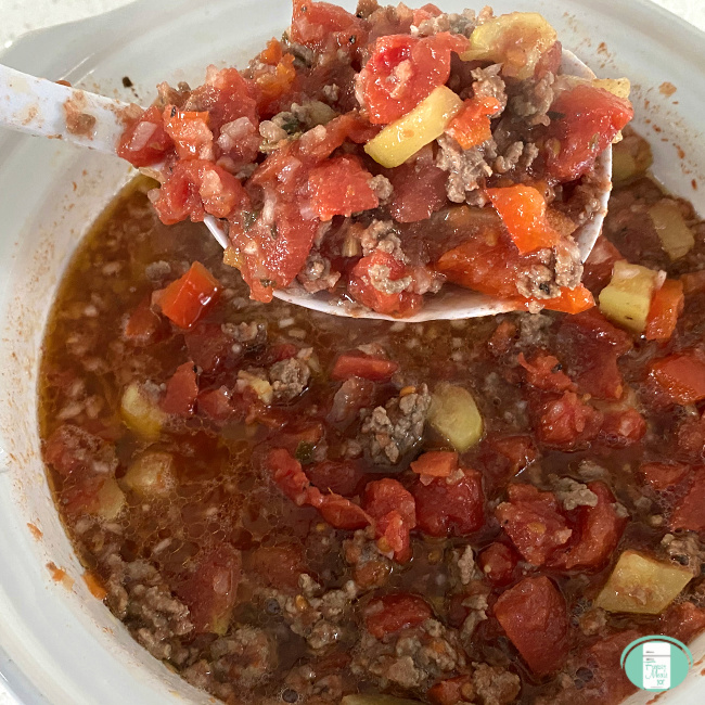 serving spoon lifting ragu beef and sausage out of a slow cooker