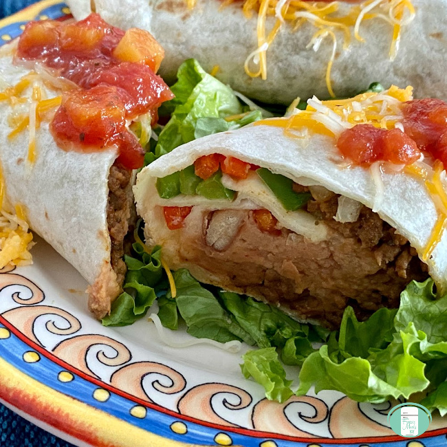 close up of a beef and bean burrito cut open and sitting on lettuce with salsa and cheese on top