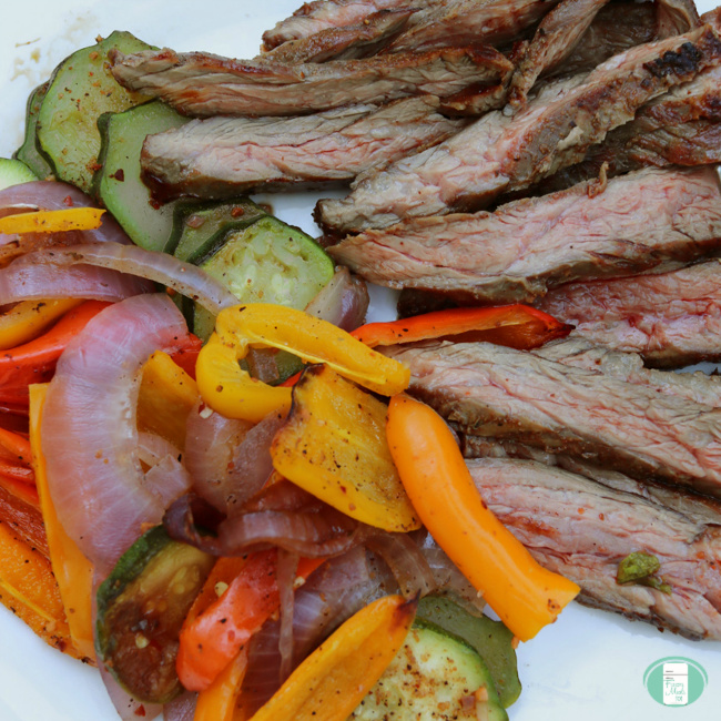 close up of grilled flank steak with onions, peppers and zucchini