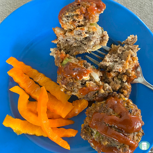 plate with a meatloaf muffin whole, drizzled in BBQ sauce and one cut up, with orange pepper strips on the side