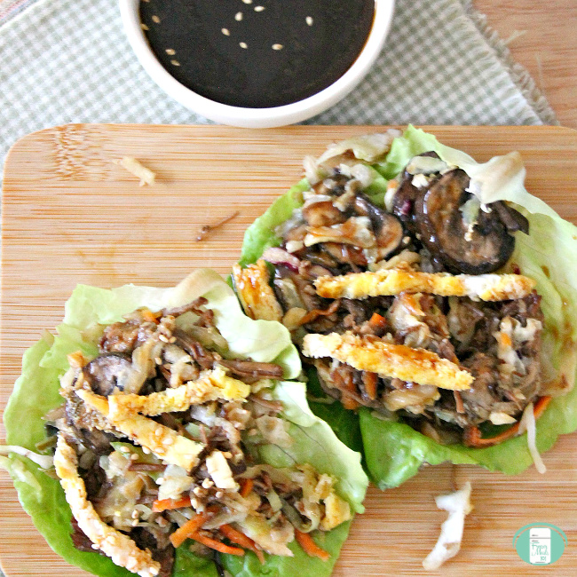 two moo shu beef lettuce wraps on a cutting board with sauce in a bowl on the side