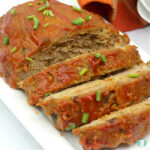sliced turkey meatloaf topped with sliced green onions on a white plate