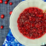 white bowl with red cranberry sauce, cranberries sprinkled nearby