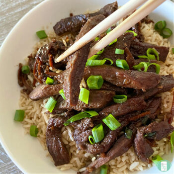 white bowl with rice, beef strips, green onions, and chopsticks