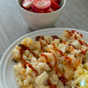 plate of hash browns topped with ketchup. A bowl of strawberries are nearby.
