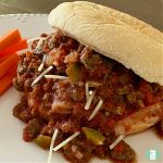 bun filled with sloppy joes mixture on a plate next to carrots