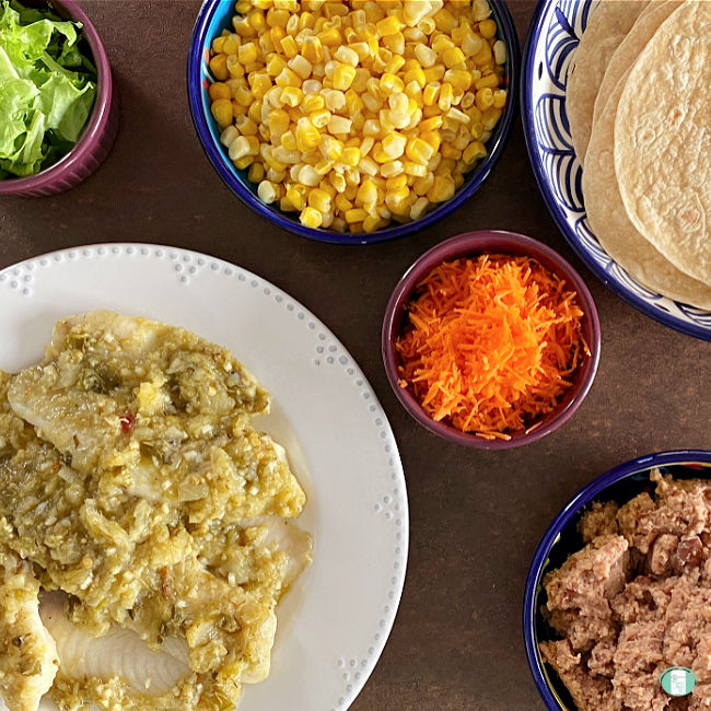 plate of fish, cooked corn, flour tortillas, shredded carrots, refried beans, lettuce