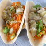 two fish tacos with shredded carrots and lettuce