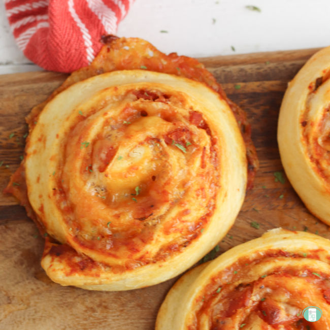 three baked pizza pinwheels on a wooden board