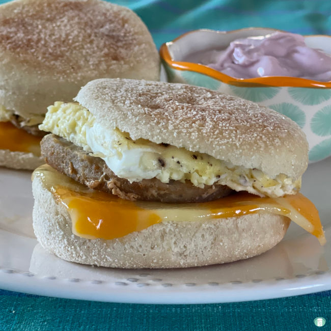 two breakfast sandwiches on a plate next to a bowl of yogurt