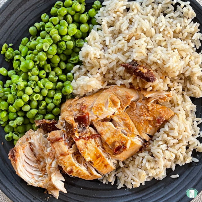 chicken, rice, and peas sit on a grey plate