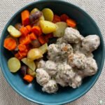 blue bowl with meatballs in white sauce next to vegetables