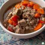 white bowl with chunks of beef and carrots and bits of barley visible