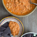 serving bowl with dip and a spoon next to blue corn chips and dip