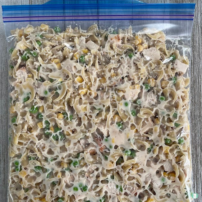 clear freezer bag filled with noodles, peas, corn, chicken 