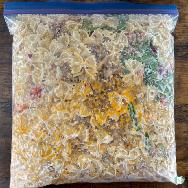 clear bag with cooked pasta, spinach, and sausage in it