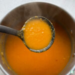 a ladle lifting orange soup out of a pot with steam rising up