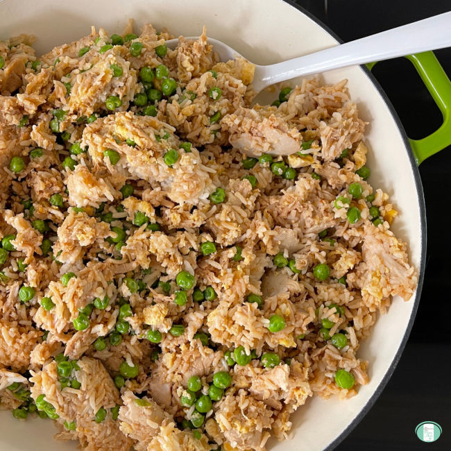 fried rice with chicken and peas in a skillet with a spatula