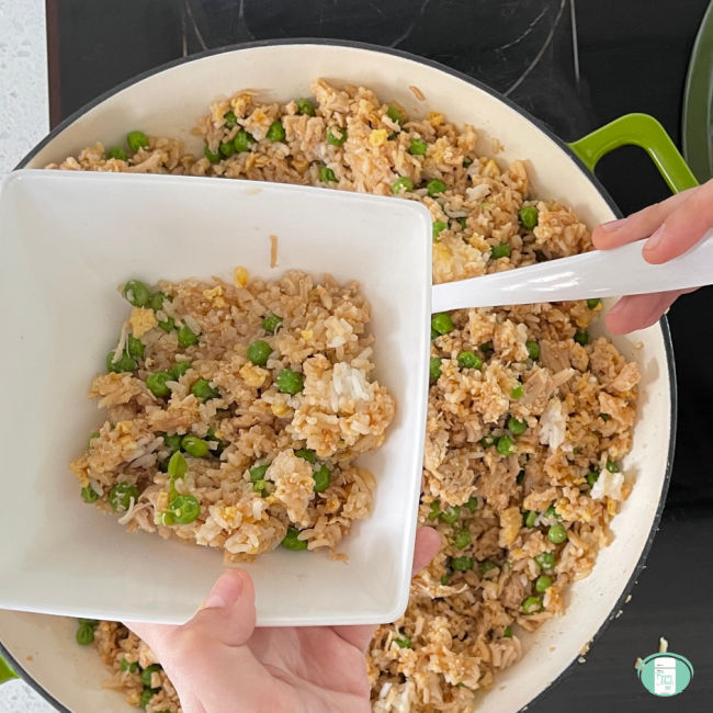 fried rice being scooped from a skillet into a white square bowl