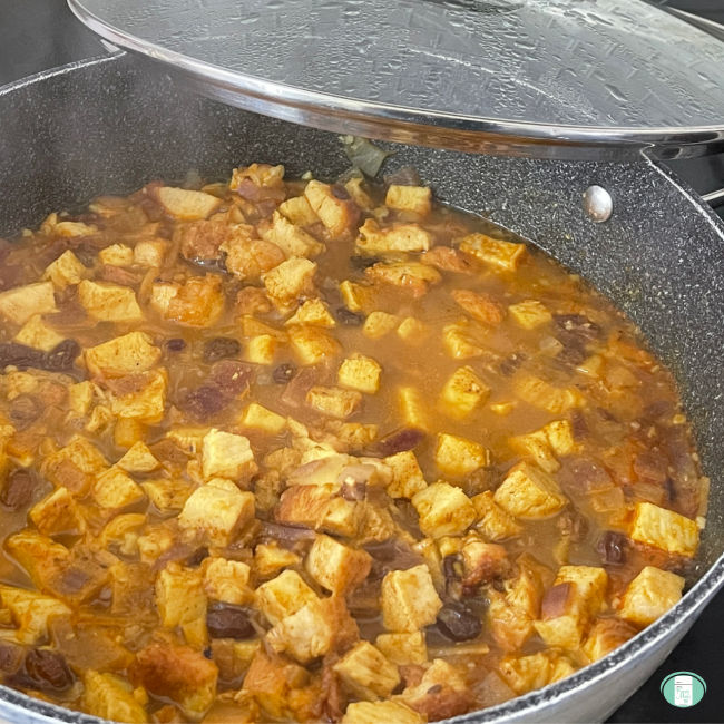 cubes of chicken in sauce in a skillet with the lid partially on