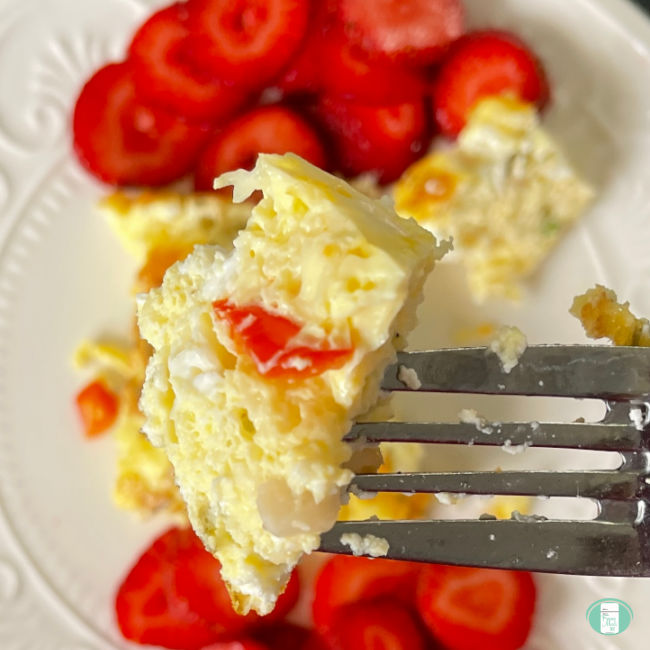 bite of frittata on a fork with sliced strawberries visible in the background