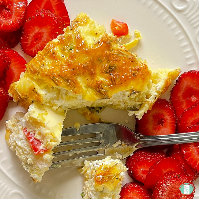 egg frittata square being cut with a fork next to sliced strawberries