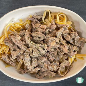 white casserole dish filled with noodles topped with beef stroganoff