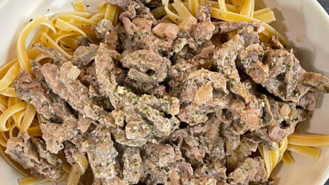 white casserole dish filled with noodles topped with beef stroganoff