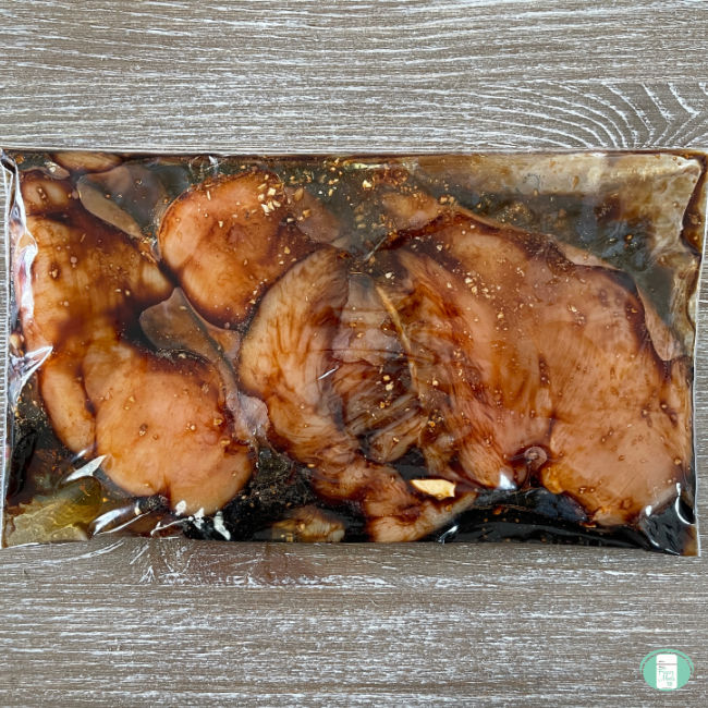 chicken marinating in a dark brown sauce in a clear bag