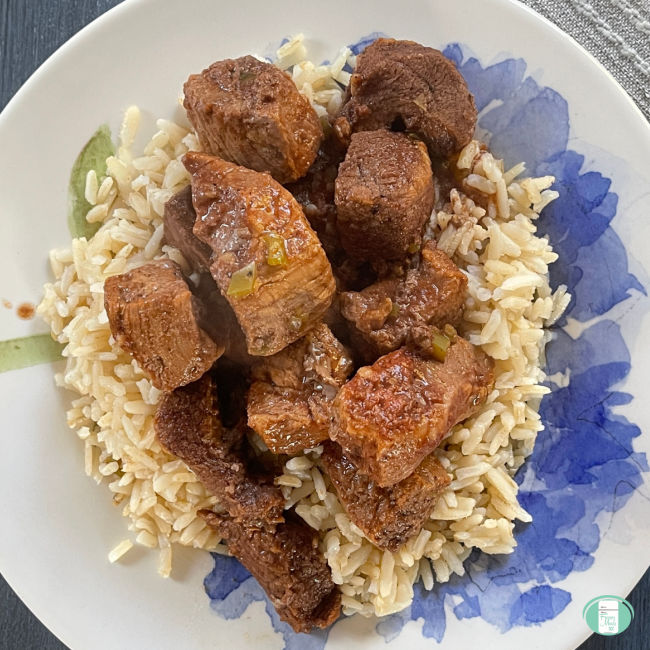 beef cubes on rice on a white and blue plate