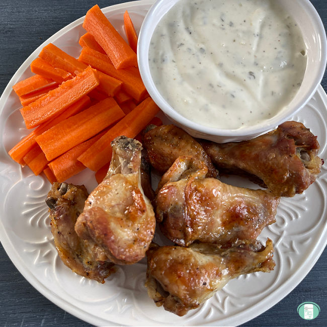 chicken wings and carrot sticks with dip on a white plate