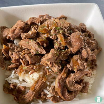 beef strips on rice in a white square bowl