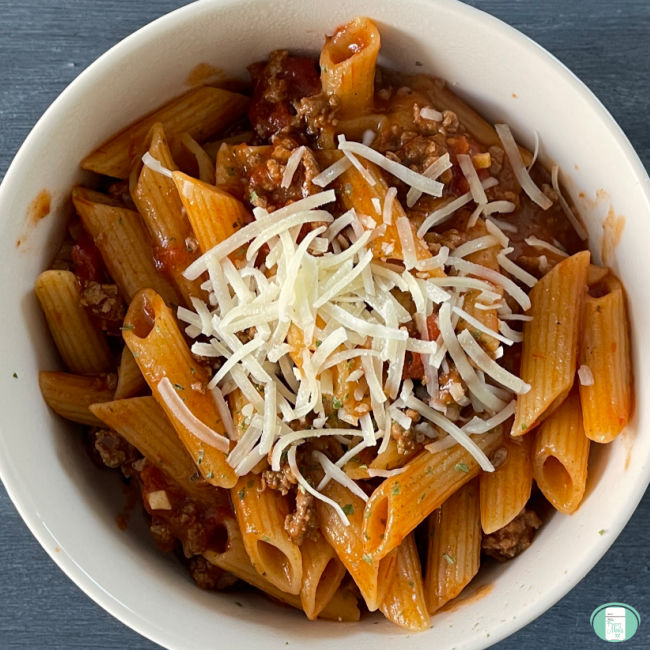white bowl of pasta with meat sauce topped with cheese