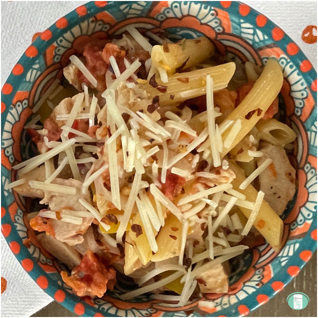 penne pasta topped with shredded Parmesan cheese in a colorful bowl