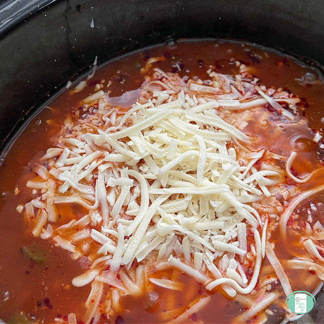 red soup in black slow cooker topped with shredded mozzarella cheese
