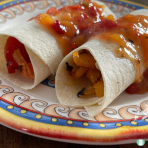two flour tortillas rolled and filled with peppers and shrimp topped with salsa