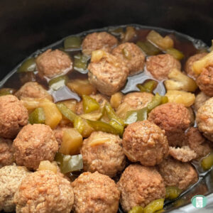 slow cooker filled with meatballs, sauce, pineapple, and green pepper pieces